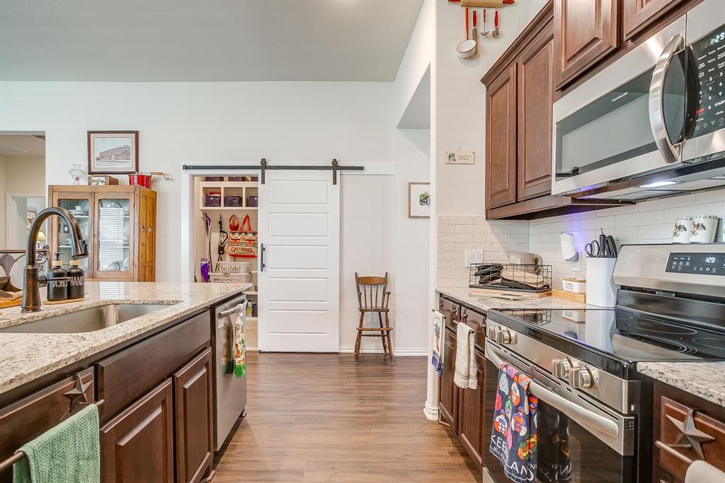 1328 San Marcus Drive Springtown, TX 76082 - Photo 11 of 37 Kitchen featuring stainless steel appliances, a barn door, light stone countertops, dark brown cabinetry, and backsplash