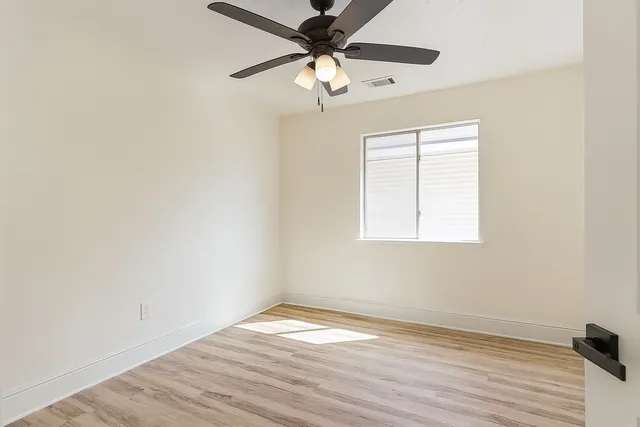 an empty room with wooden floor chandelier fan and windows