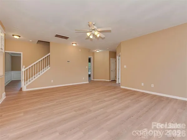 a view of an empty room with wooden floor and a ceiling fan