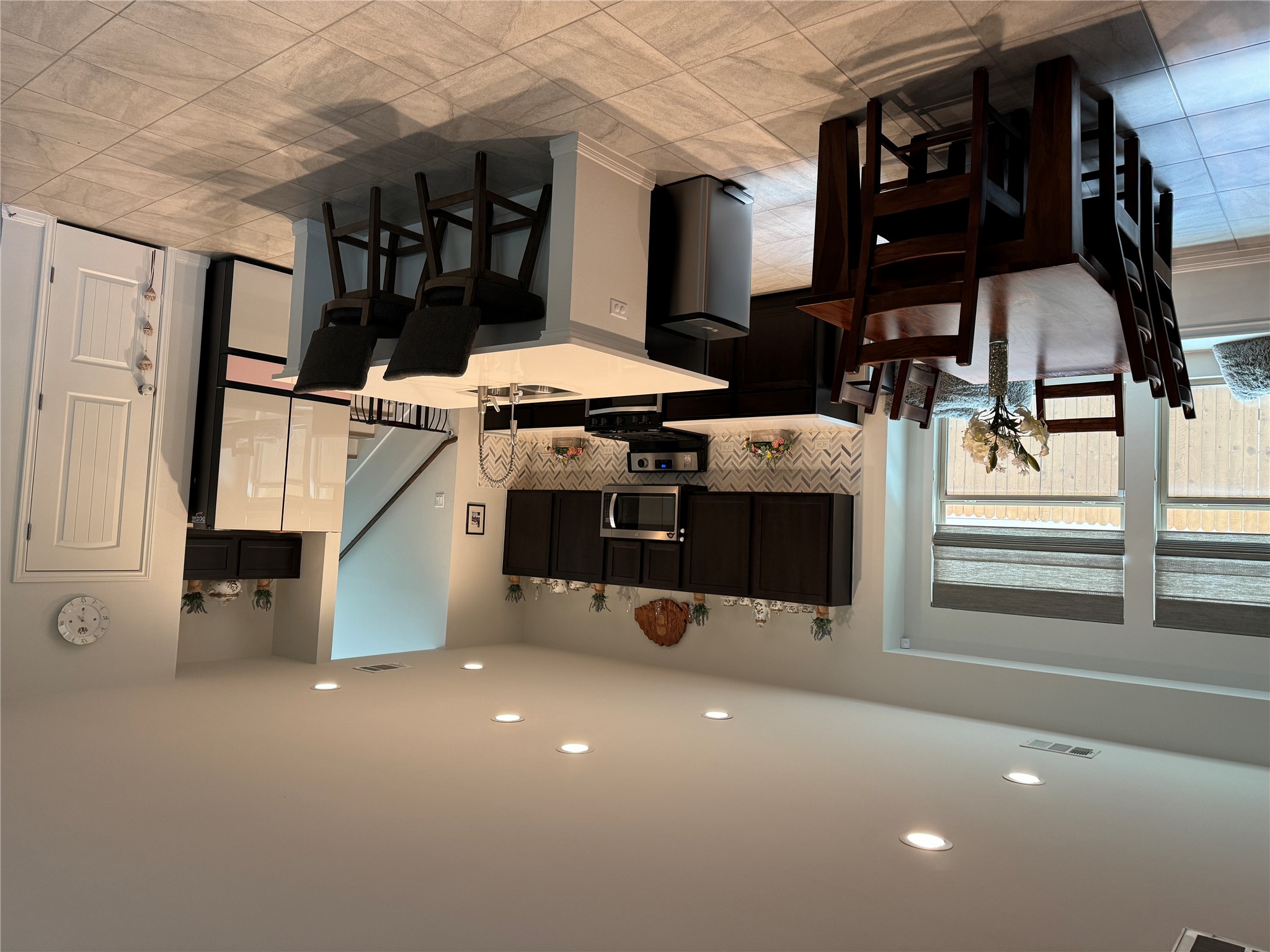 Open-concept kitchen and dining area featuring a central island with seating, dark wood-finish cabinetry, a herringbone tile backsplash, recessed lighting, and large format floor tiling