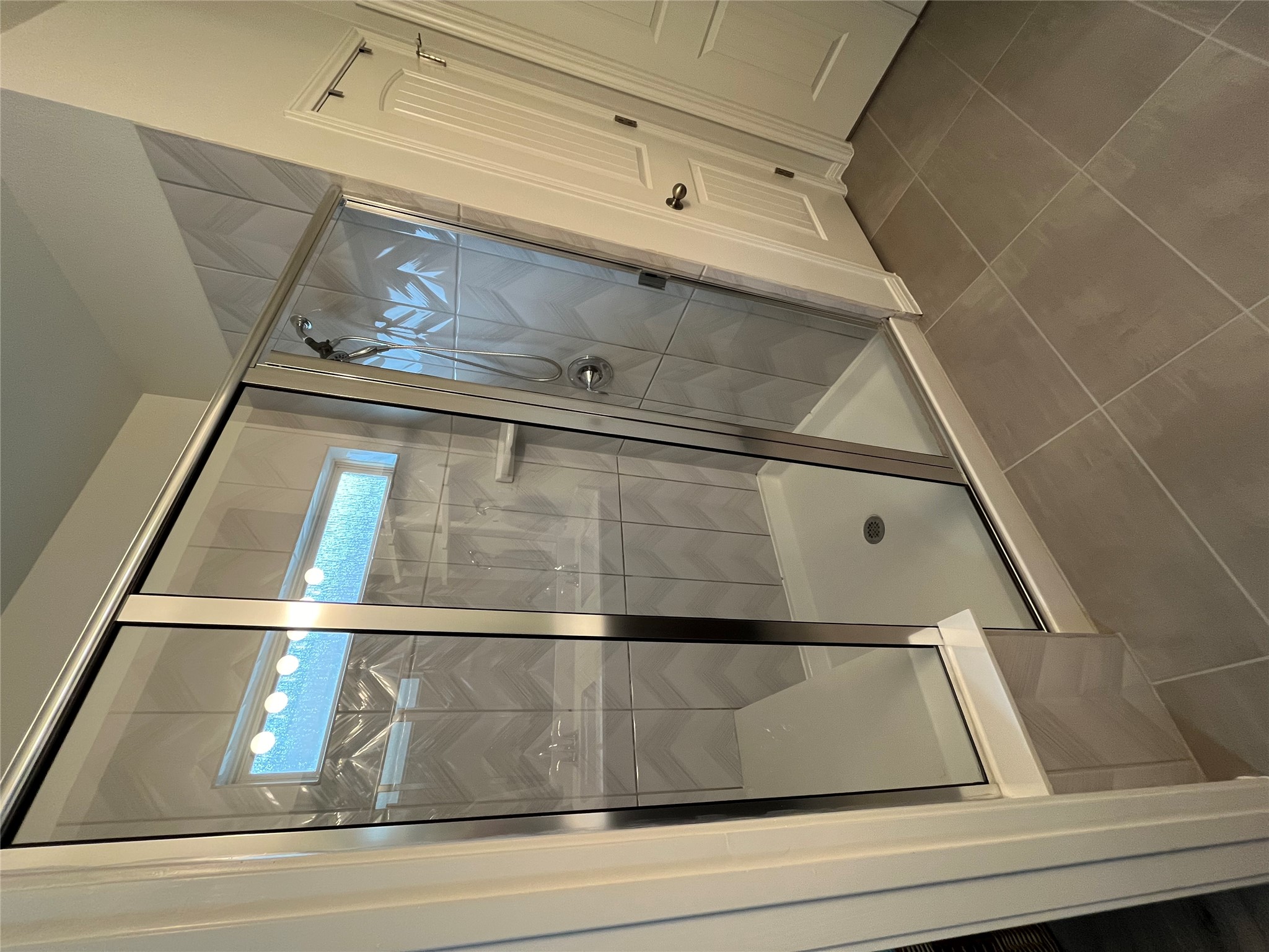 8145 Daisy Cutter Crossing Georgetown, TX 78626 - Photo 13 of 25 Glass-enclosed shower featuring a built-in bench, herringbone pattern wall tiles, a horizontal window, and a chrome shower fixture