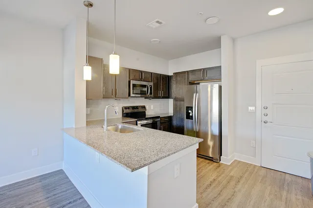 a kitchen with granite countertop a refrigerator a sink a stove a microwave and wooden floor