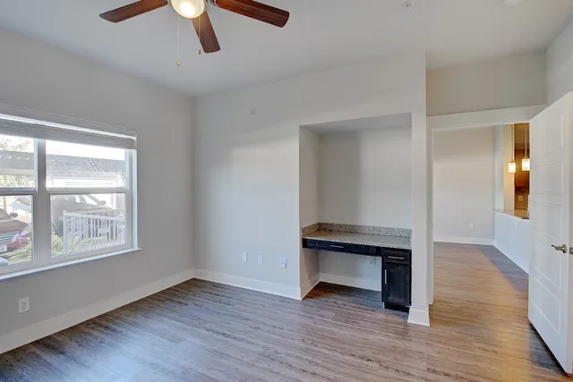 an empty room with wooden floor fan and windows