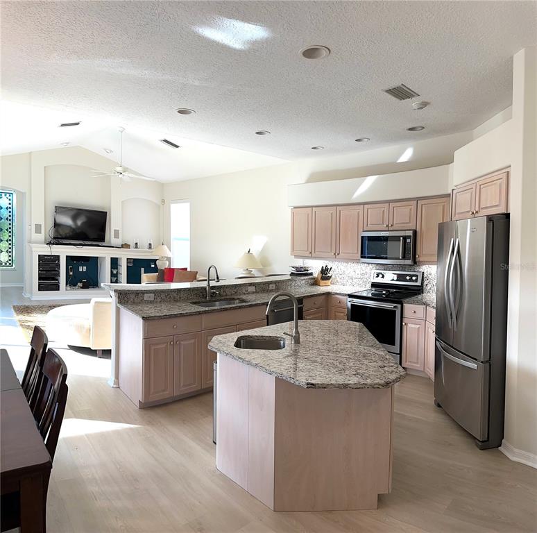 8870 Huntington Pointe Drive Sarasota, FL 34238 - Photo 18 of 28 a kitchen with stainless steel appliances granite countertop a stove top oven a sink dishwasher a refrigerator and a dining table with wooden cabinets