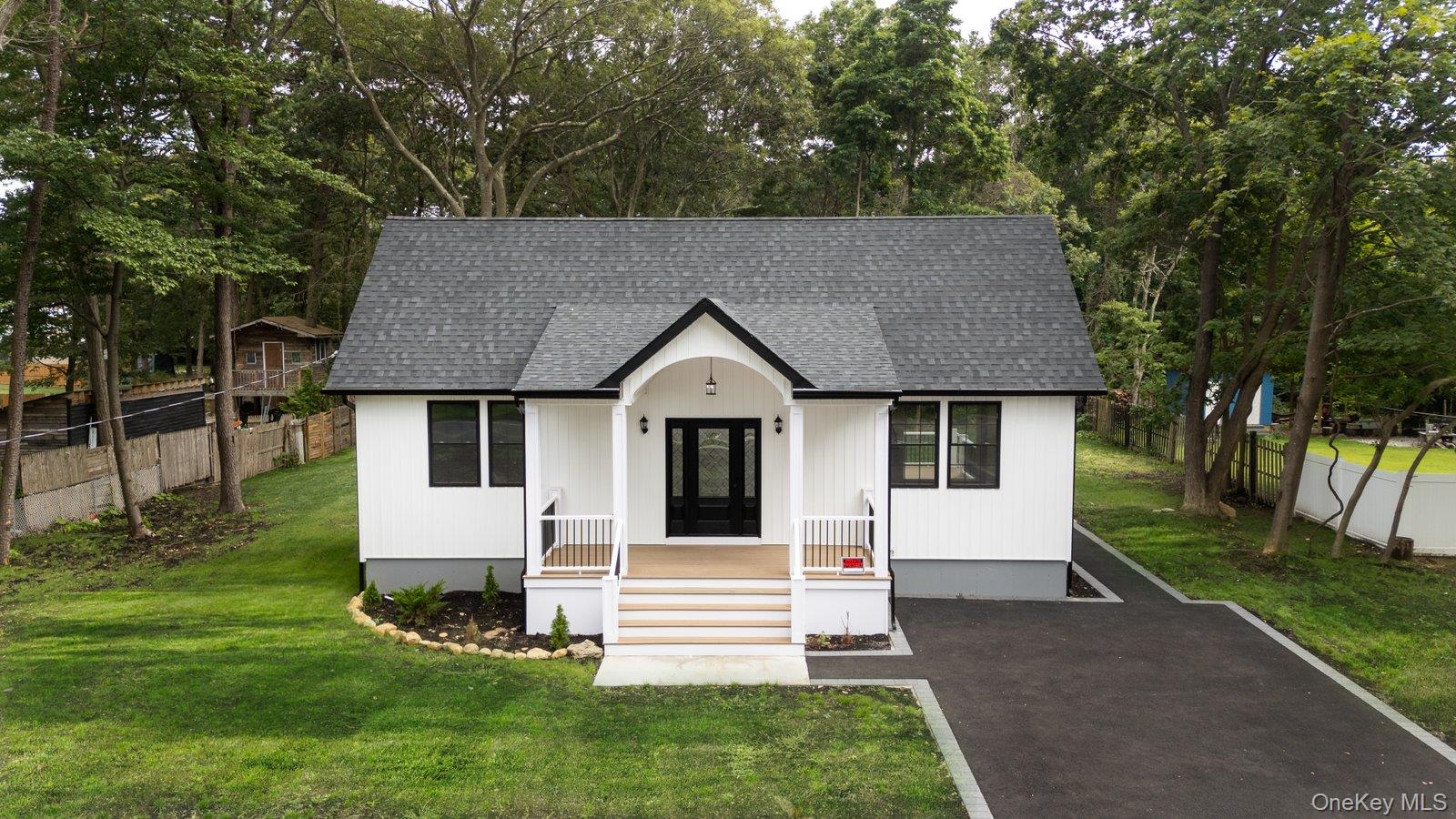 View of front facade with roof with shingles, a porch, and view of wooded area