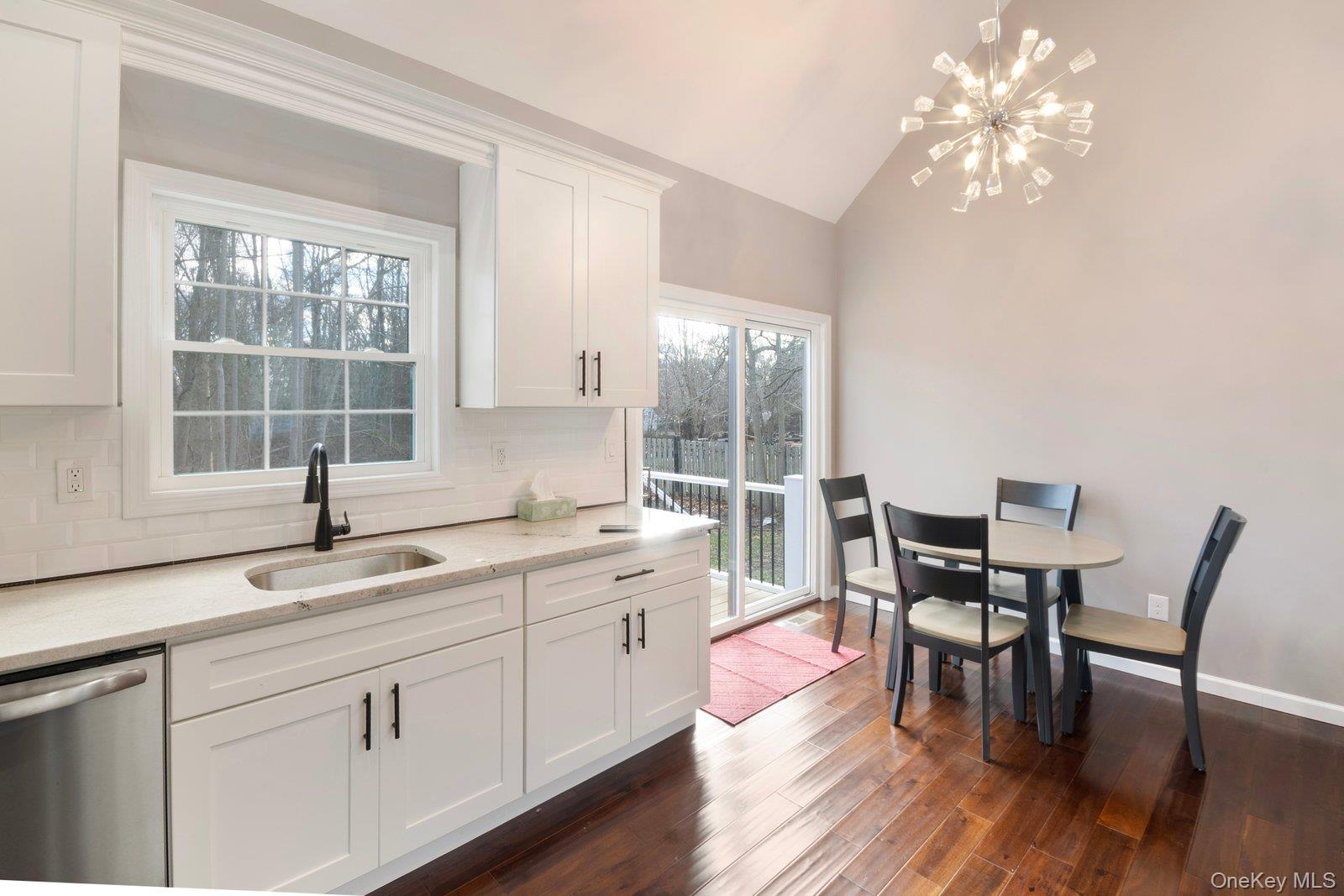 568 Granny Road Medford, NY 11763 - Photo 5 of 22 Kitchen with white cabinets, backsplash, dishwasher, light stone counters, and a chandelier