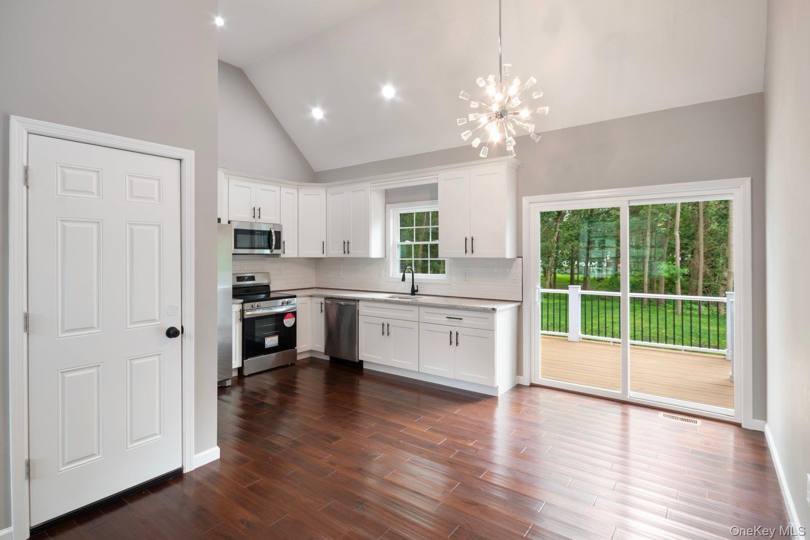 568 Granny Road Medford, NY 11763 - Photo 6 of 22 Kitchen with a chandelier, white cabinetry, appliances with stainless steel finishes, tasteful backsplash, and high vaulted ceiling