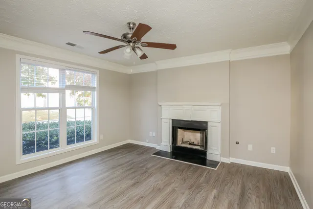 a view of an empty room with wooden floor fireplace and a window
