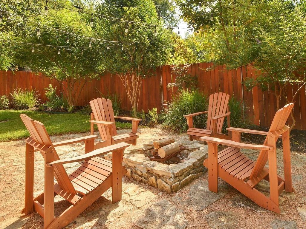 610 West N Loop Boulevard Austin, TX 78751 - Photo 25 of 29 The property features a well-maintained yard with a stone fire pit and four wooden Adirondack chairs, surrounded by lush green foliage and a wooden privacy fence