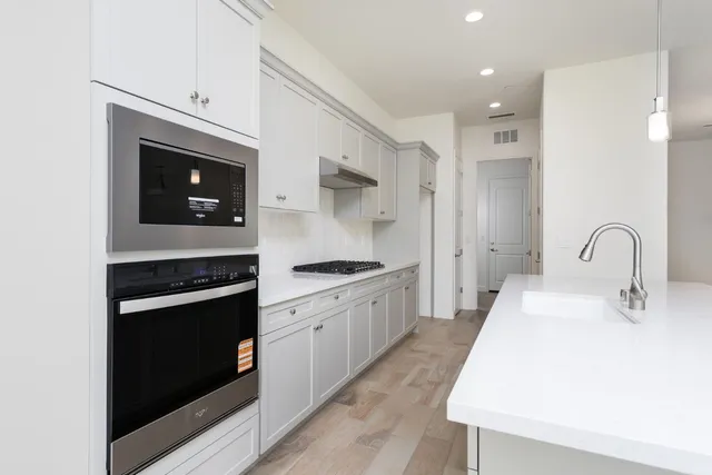 a kitchen with stainless steel appliances granite countertop a stove top oven a sink and white cabinets