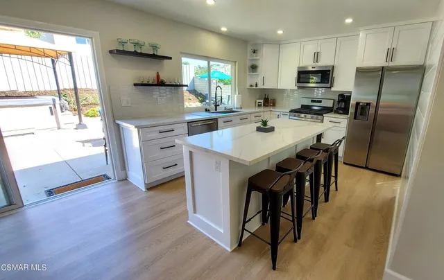 a kitchen with stainless steel appliances kitchen island granite countertop a table chairs sink refrigerator and microwave