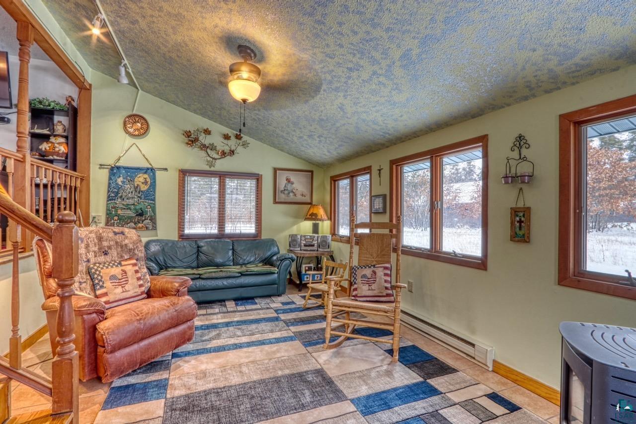 33469 No Mans Lake Road Minong, WI 54859 - Photo 8 of 38 Family room with vaulted ceiling, a baseboard radiator, and a wood pellet stove.