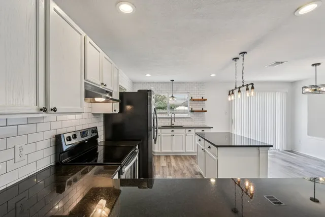 a kitchen with granite countertop a refrigerator a stove and white cabinets with wooden floor