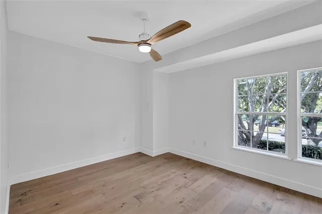 an empty room with wooden floor fan and windows