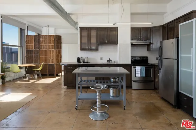 a kitchen with stainless steel appliances a refrigerator a stove a sink a dining table and chairs with wooden floor