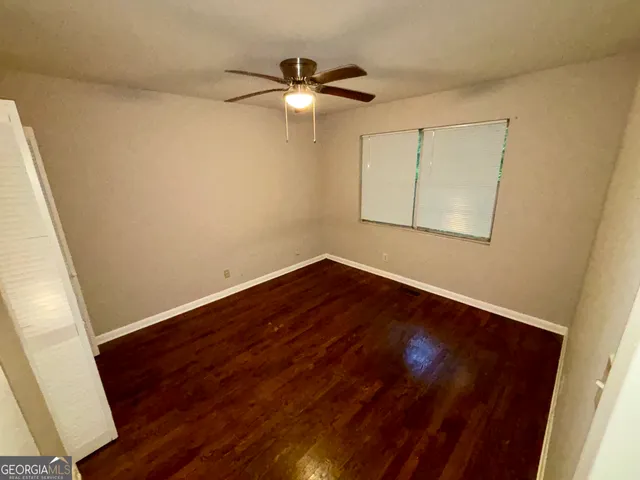 a view of an empty room with wooden floor and a ceiling fan