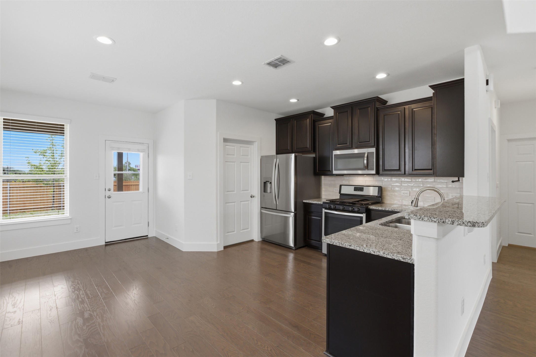 2004 Garretts Way Manchaca, TX 78652 - Photo 11 of 37 Kitchen featuring stainless steel appliances, light stone counters, a peninsula, dark wood-type flooring, and dark wood finish cabinets