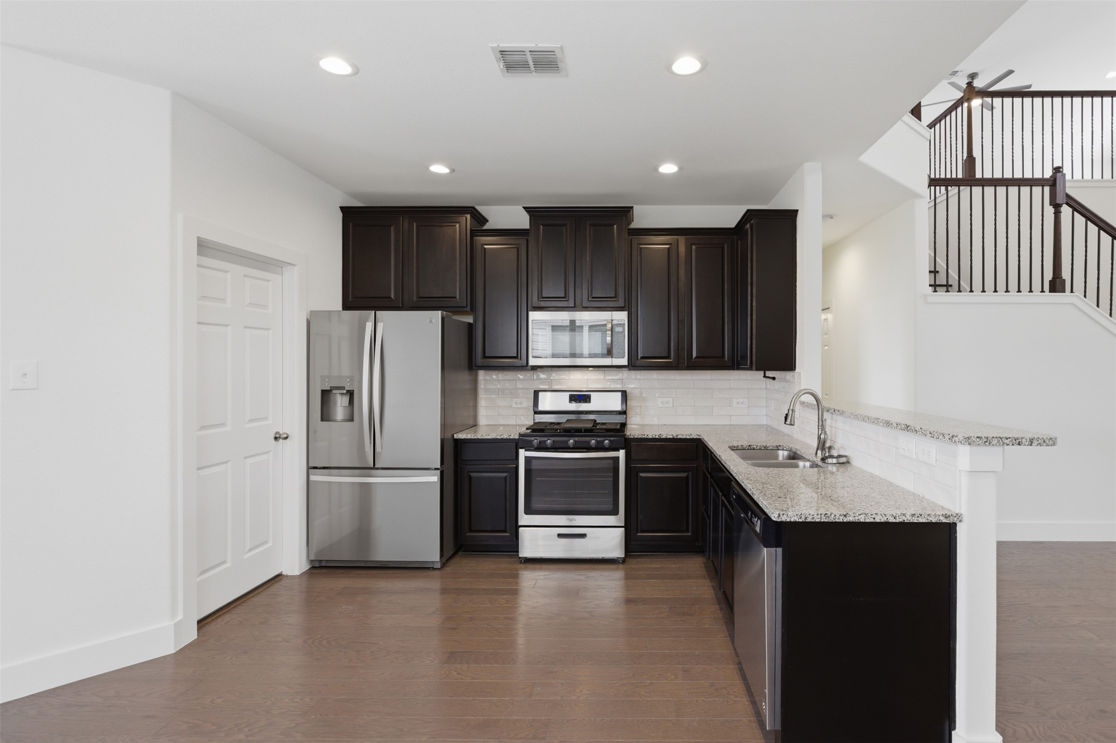 2004 Garretts Way Manchaca, TX 78652 - Photo 12 of 37 Kitchen featuring stainless steel appliances, a peninsula, dark wood-style flooring, light stone counters, and recessed lighting