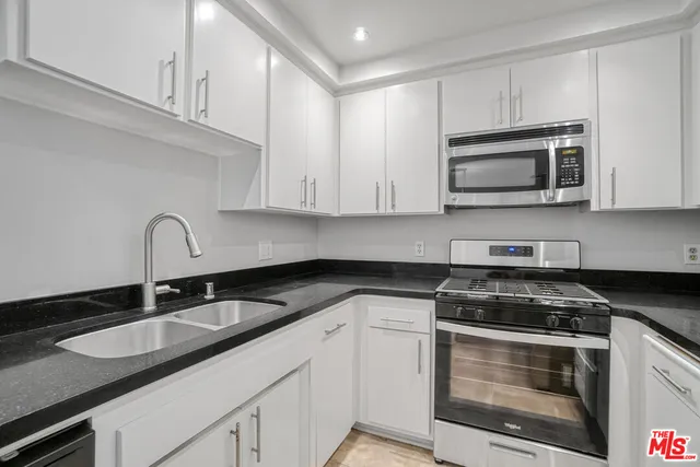 a kitchen with granite countertop a refrigerator a stove a sink and white cabinets
