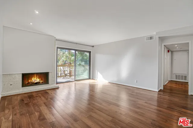 a view of an empty room with wooden floor fireplace and a window