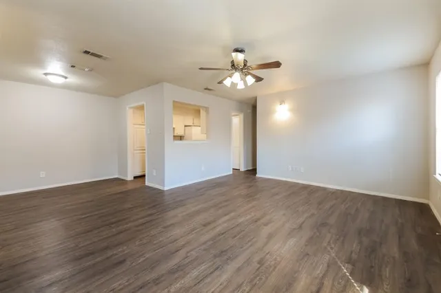 a view of an empty room with wooden floor and a ceiling fan