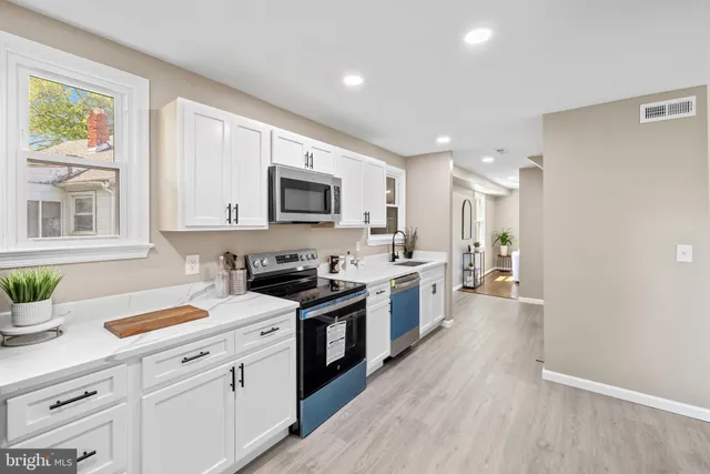 a kitchen with stainless steel appliances a sink dishwasher a stove top oven a refrigerator with white cabinets and wooden floor