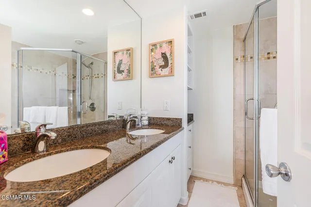 a bathroom with a granite countertop double vanity sink mirror and shower