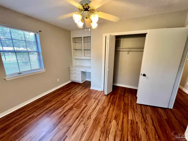 an empty room with wooden floor chandelier fan and windows