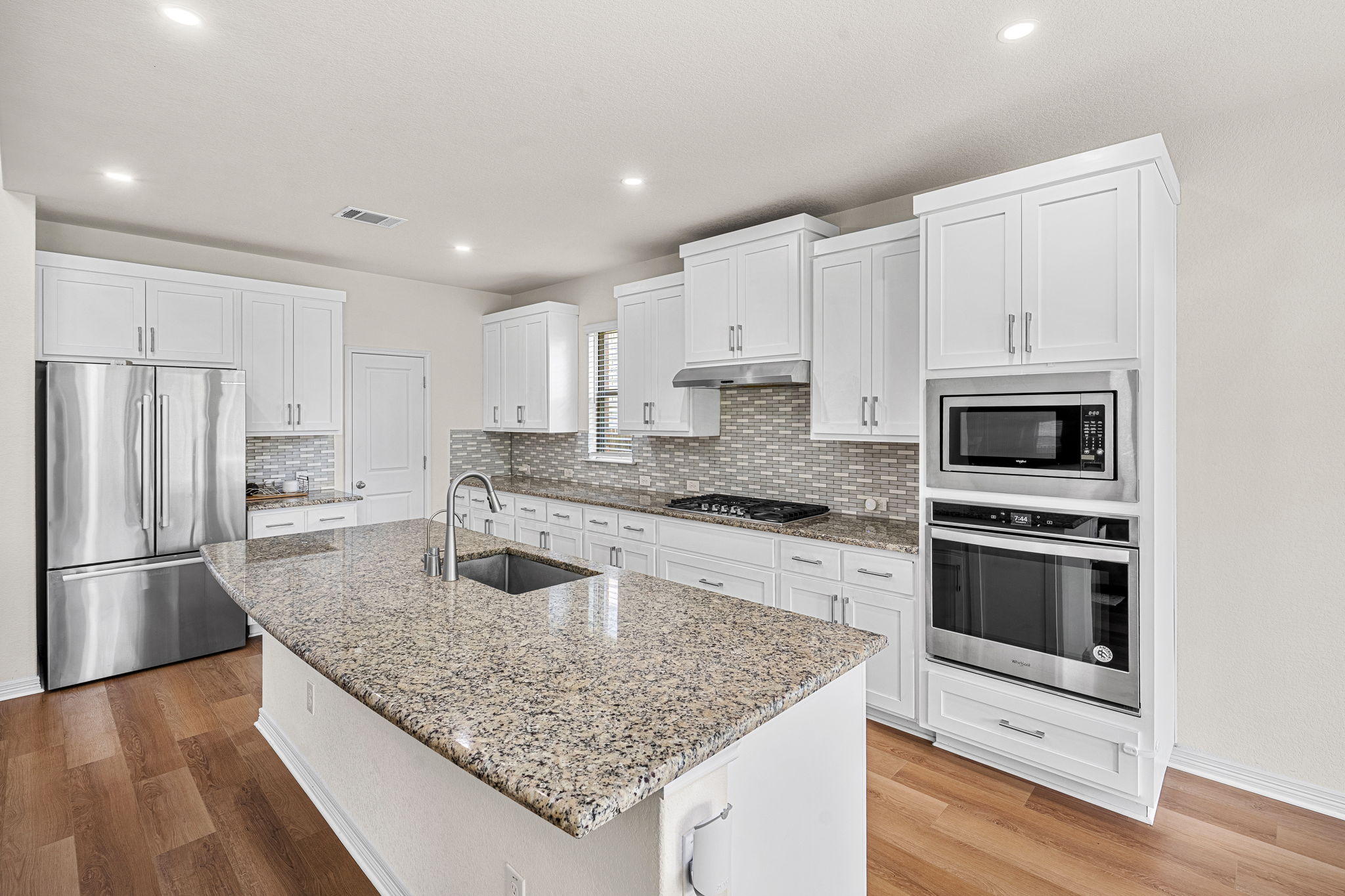 20813 Carries Ranch Road Pflugerville, TX 78660 - Photo 13 of 40 Rich wood flooring grounds this modern culinary space featuring premium stone countertops and white cabinetry.