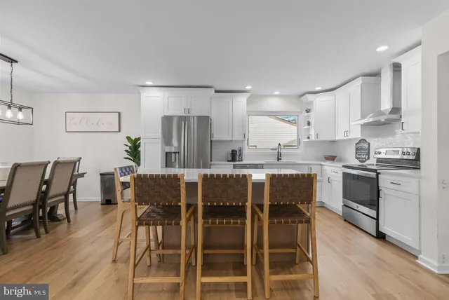 a kitchen with stainless steel appliances a stove a sink dishwasher a refrigerator with white cabinets and wooden floor