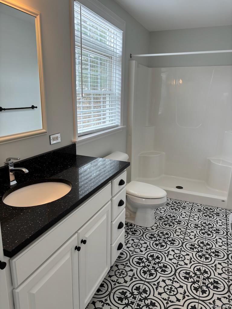 1661 Old Country Road, Unit 539 Riverhead, NY 11901 - Photo 12 of 26 a bathroom with a granite countertop sink a toilet a mirror a vanity a window and shower