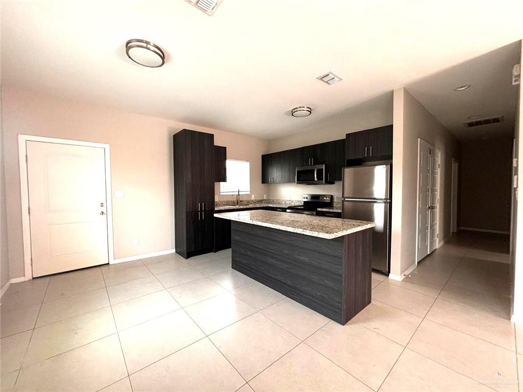 1405 Alta Vista Drive, Unit 4 Weslaco, TX 78596 - Photo 3 of 15 Kitchen featuring stainless steel appliances, a center island, light tile patterned flooring, dark cabinetry, and light stone countertops