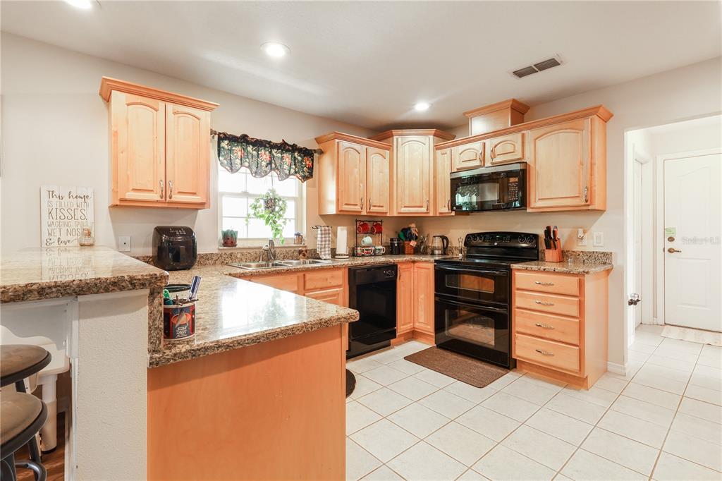 7290 Northeast 106 Terrace Bronson, FL 32621 - Photo 19 of 40 a kitchen with stainless steel appliances granite countertop a stove top oven a sink dishwasher a dining table and chairs with wooden floor