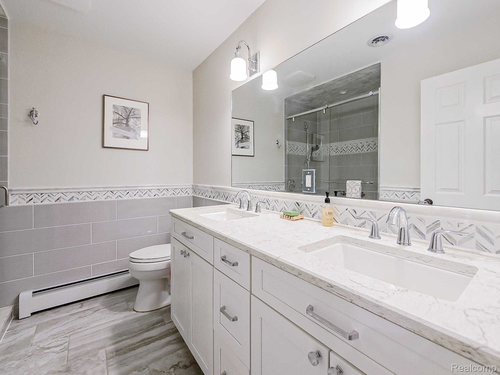 3720 East Clarkston Road Oakland, MI 48363 - Photo 16 of 60 Full bathroom featuring a stall shower, a baseboard heating unit, double vanity, tile walls, and a wainscoted wall
