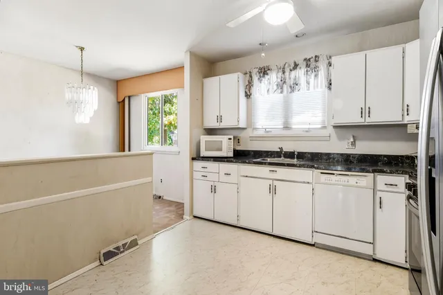 a kitchen with granite countertop white cabinets white appliances a sink and a large window