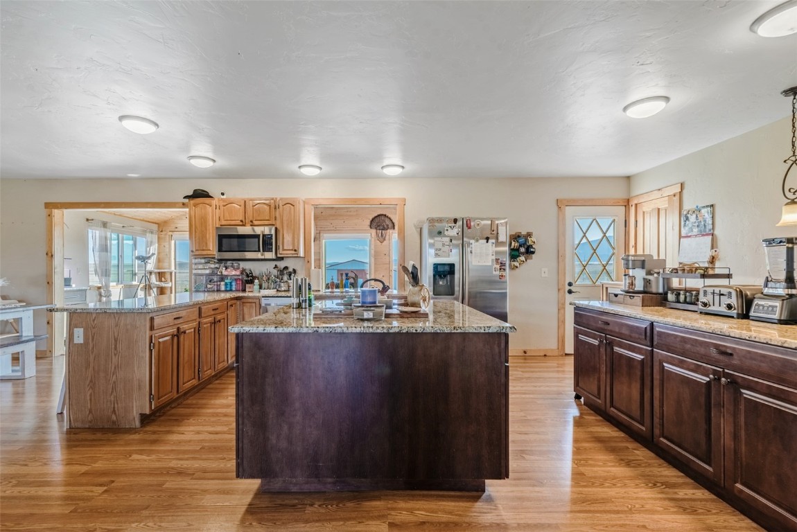 465 Litmer Road Jefferson, CO 80456 - Photo 19 of 50 Kitchen featuring appliances with stainless steel finishes, an island with sink, light wood finished floors, light stone counters, and healthy amount of natural light