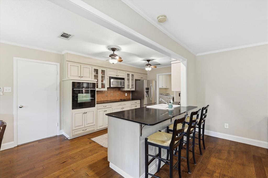 7200 Tamarack Road Benbrook, TX 76116 - Photo 11 of 38 Galley kitchen featuring wood-finish flooring, an island with countertop seating, built-in wall oven and microwave.