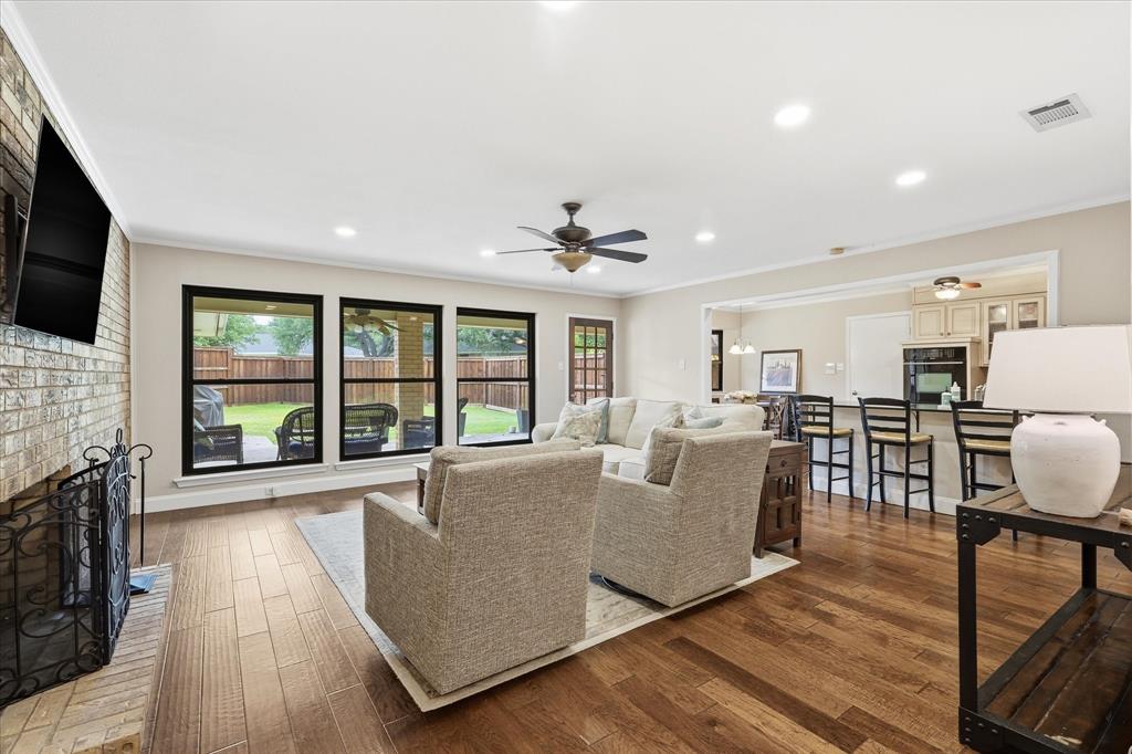 7200 Tamarack Road Benbrook, TX 76116 - Photo 6 of 38 Spacious living room featuring wood-finish flooring, and a brick wood burning fireplace connected to galley kitchen with counter seating.