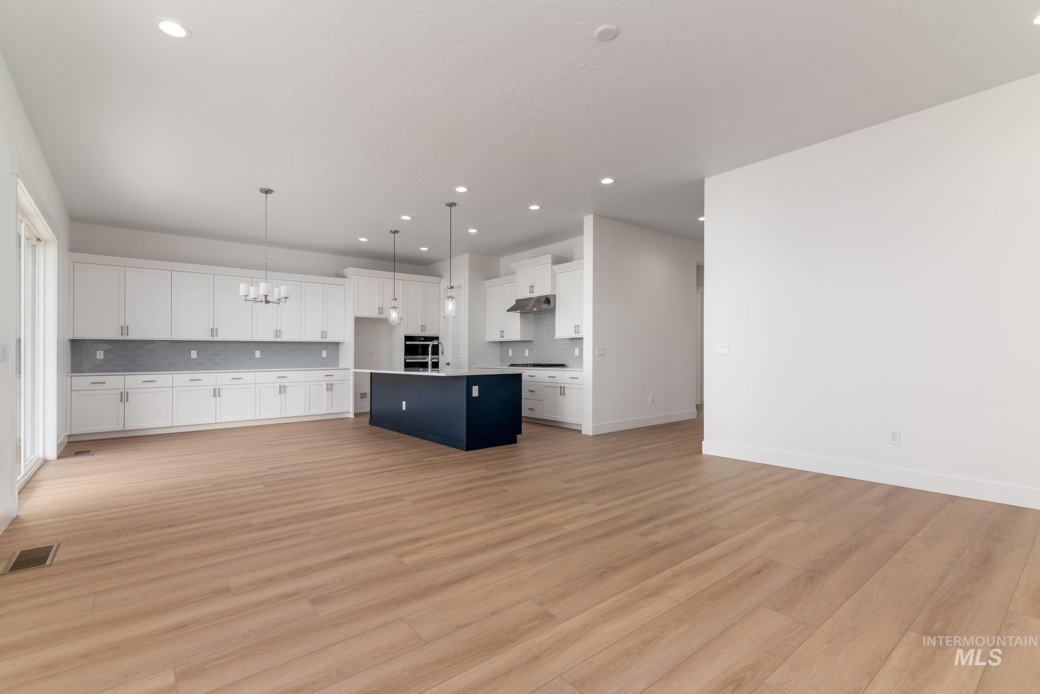 1195 West Switchgrass Drive Meridian, ID 83642 - Photo 4 of 22 Open-concept living space featuring wood-finish flooring, a kitchen with white cabinetry, a contrasting dark-toned kitchen island, and recessed lighting