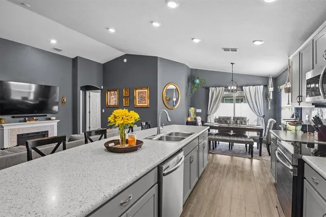 a kitchen with stainless steel appliances kitchen island granite countertop a stove a sink dishwasher a dining table and chairs with wooden floor