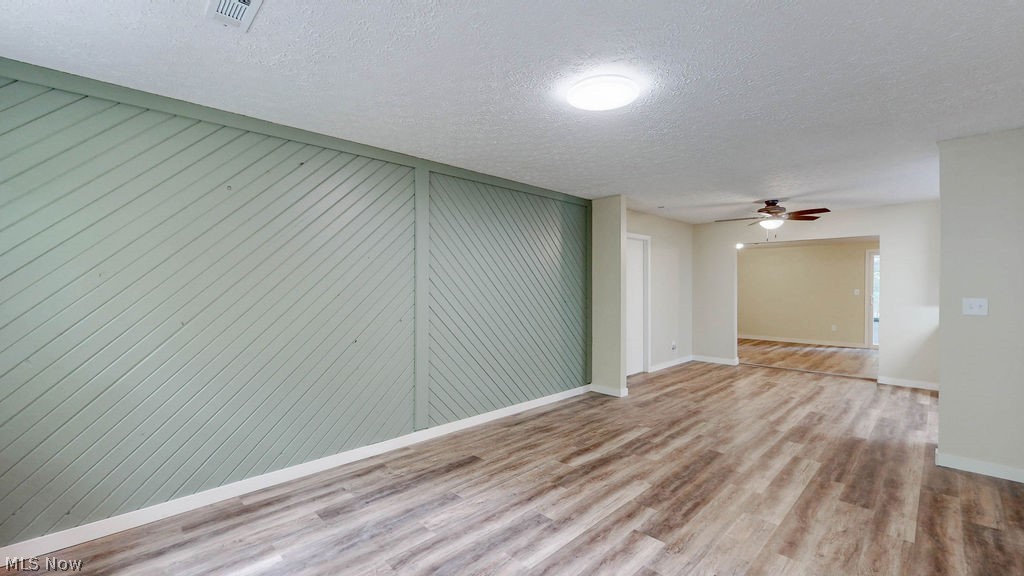 Spacious interior featuring wood-finish flooring, a decorative accent wall with diagonal paneling, and neutral wall tones