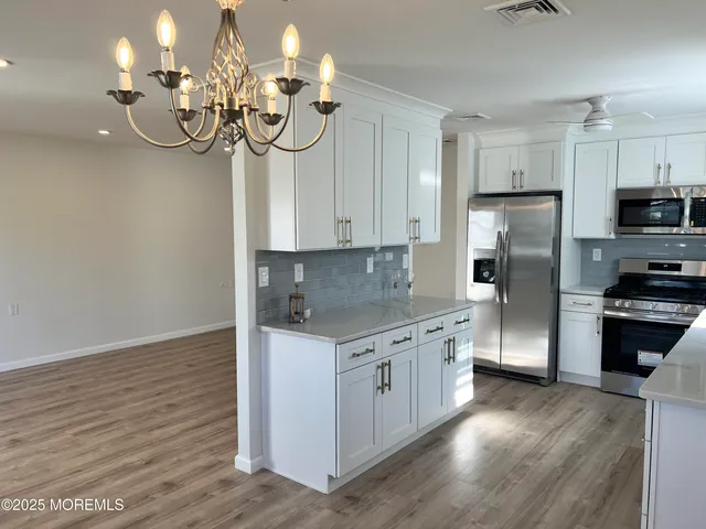 a kitchen with stainless steel appliances granite countertop a refrigerator a sink dishwasher a stove and a dining table with wooden floor