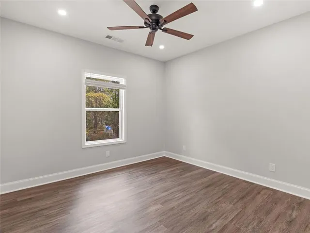 an empty room with wooden floor ceiling fan and windows