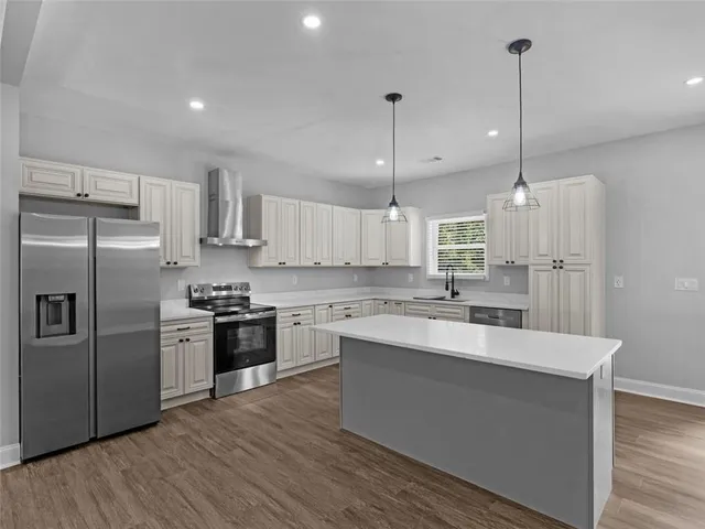 a kitchen with stainless steel appliances kitchen island granite countertop a sink a stove a refrigerator and island with wooden floor