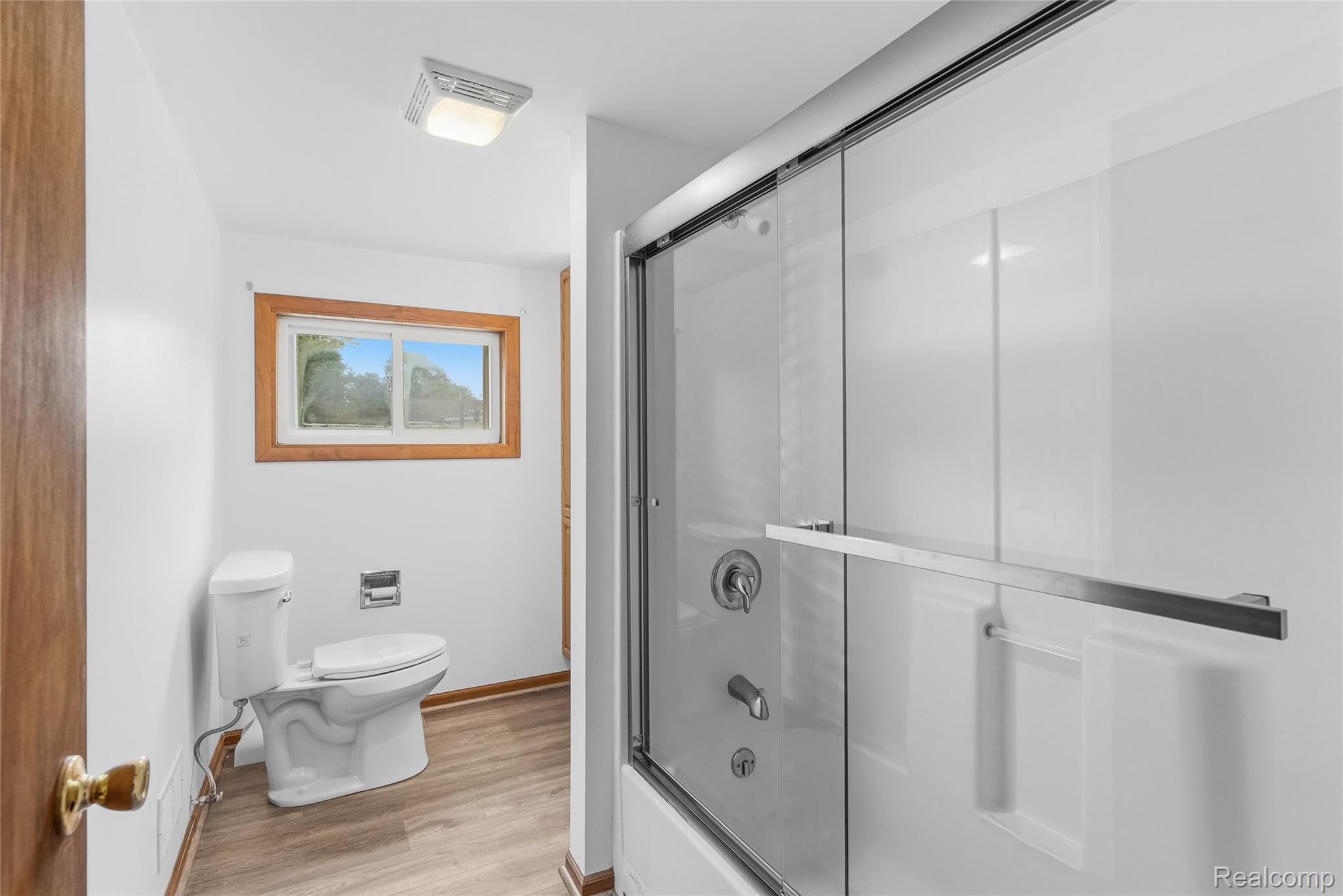 1843 Curtis Road Birch Run, MI 48415 - Photo 19 of 25 Bathroom featuring a white toilet, wood-finish flooring, a window with natural wood trim, and a shower with a sliding glass door
