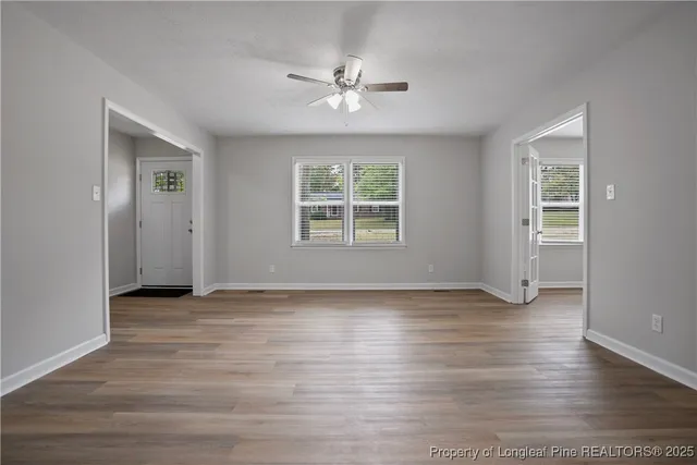 an empty room with wooden floor chandelier and windows