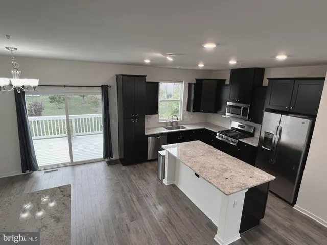 a kitchen with stainless steel appliances kitchen island granite countertop a refrigerator a sink dishwasher and a stove with wooden floor