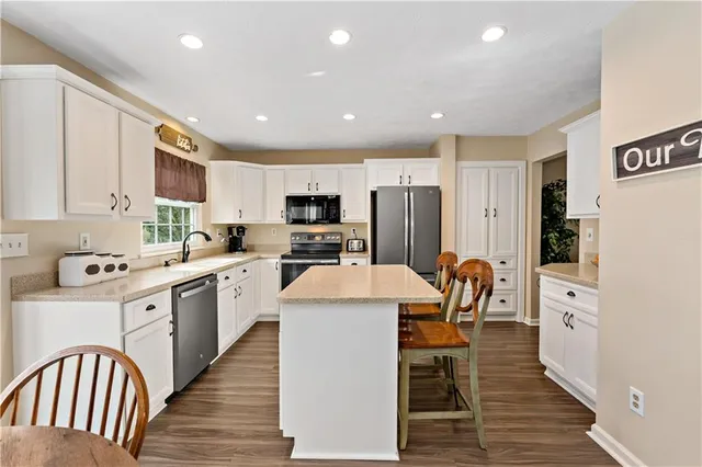 a kitchen with stainless steel appliances a refrigerator a stove top oven a sink dishwasher a dining table and chairs with wooden floor