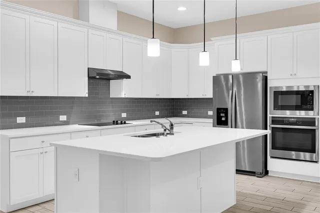 a kitchen with stainless steel appliances a sink a stove a refrigerator a center island and cabinets