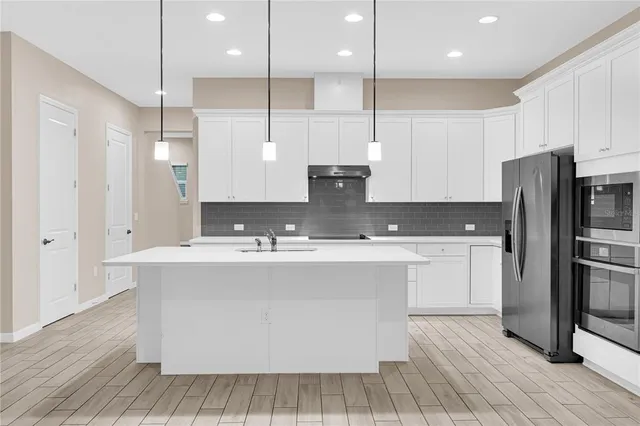 a large kitchen with stainless steel appliances a large counter top a sink a refrigerator and a cabinets